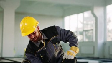 İnşaat alanında kameranın önünde genç bir inşaat işçisi inşaat malzemelerini fırçayla boyuyor koruyucu kask ve üniforma giyiyor. 4k