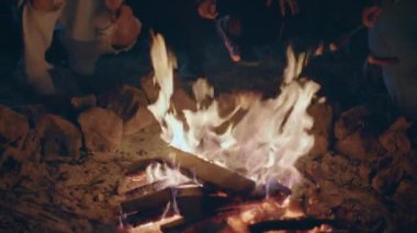 Doğanın ortasında, kamp alanındaki yangın kazığında sosis pişiren bir grup arkadaşa yakın olarak gecenin tadını çıkarın. 4k
