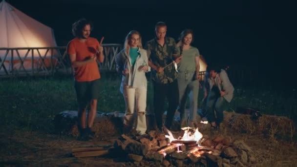 在火堆前的摄像机前 在大自然的中央 在营地里 迷人的女士们和小伙子们在一起玩的很开心 他们吃了些腊肠 在火堆前准备好了 — 图库视频影像