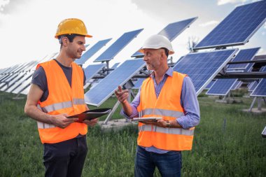 Güneş enerjisi üreten fotovoltaik alanda genç bir teknisyen ve yatırımcı güneşin işleyişini analiz ediyor fotovoltaik güneş panellerinin temizliği hakkında tartışıyorlar..