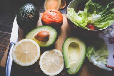 fresh avocado, lettuce with lemon and other ingredients on wooden background 