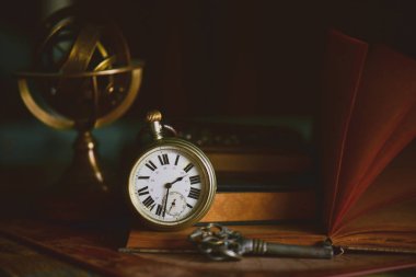 old books with clock and key on wooden table 