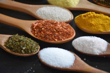 various spices in wooden spoons on a black background