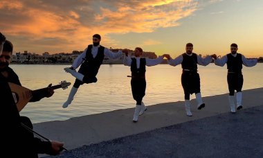 RETHYMNO, CRETE, GREECE - 17 Haziran 2021: Genç Yunan dansçılar, Rethymno Marina limanında Yunan halk müziği eşliğinde geleneksel bir dans sergilediler. Gün batımı ışığı.