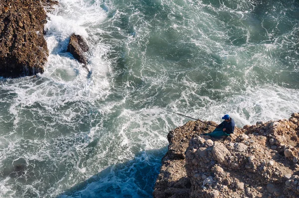 A man with a fishing rod is fishing on the rocks near the sea. Active recreation in nature. — Foto Stock