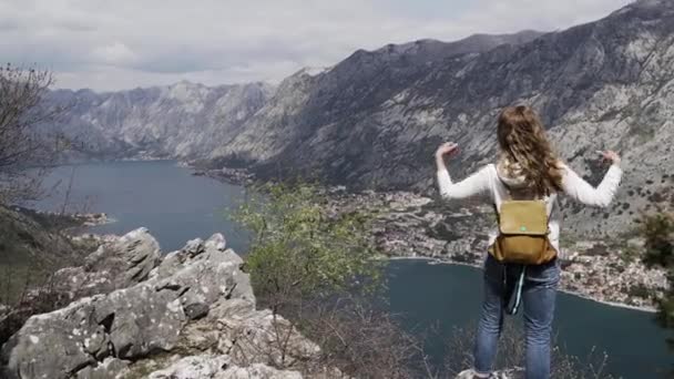 Une fille avec un sac à dos se trouve au sommet d'une montagne au Monténégro — Video