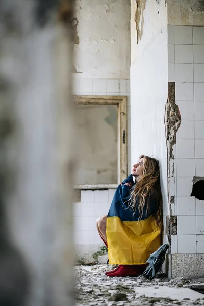 Una mujer ucraniana en una casa arruinada. Bandera de Ucrania. Alto a la guerra — Foto de Stock