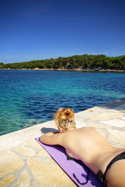 Ung rødhåret kvinde solbadning på stranden ved klart hav, Kroatien Dalmatien - Stock-foto