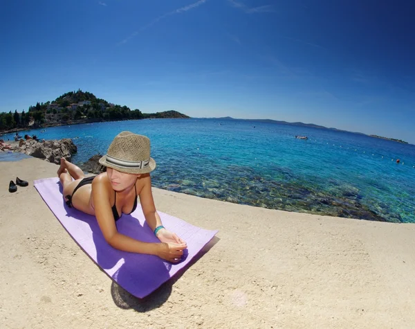 Jonge vrouw in stro hoed zonnebaden op een strand — Stockfoto