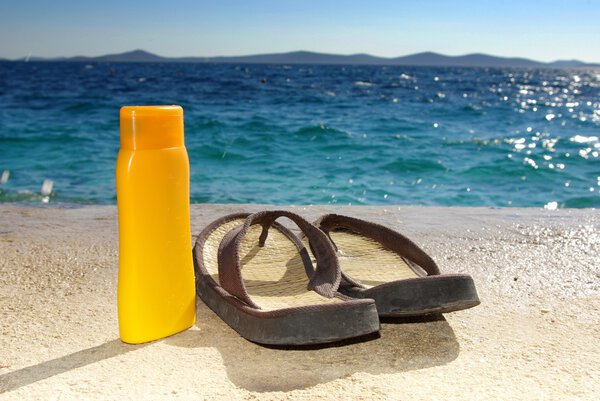 Suntan cream or oil and sandals on beach