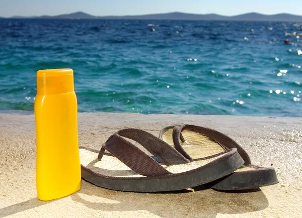 Crema bronceadora o aceite y sandalias en la playa — Foto de Stock