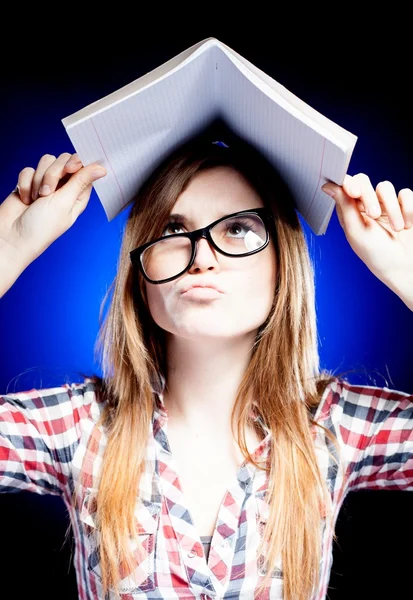 Chica joven confundida y desconcertada sosteniendo libro de ejercicios en su cabeza —  Fotos de Stock