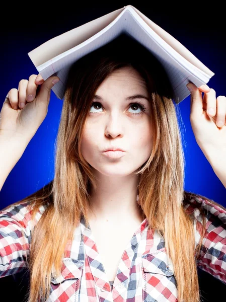 Confuso e perplesso giovane ragazza tenendo libro di esercizi sulla testa — Foto Stock