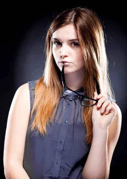 Junge Frau beißt mit interessiertem Blick in Nerd-Brille — Stockfoto