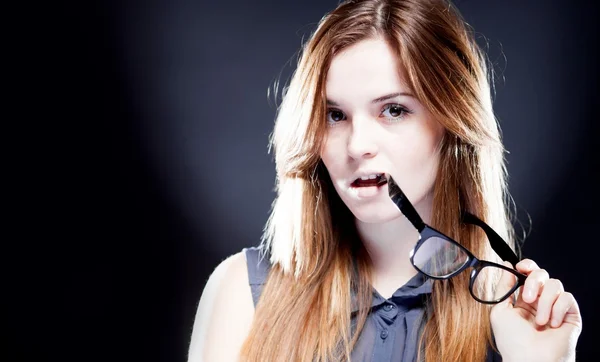 Junge Frau beißt mit interessiertem Blick in Nerd-Brille — Stockfoto