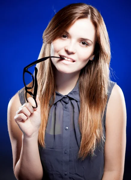 Junge Frau beißt mit interessiertem Blick in Nerd-Brille — Stockfoto