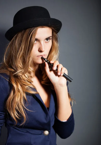 Elegante mujer fumando cigarrillo electrónico con traje y sombrero —  Fotos de Stock