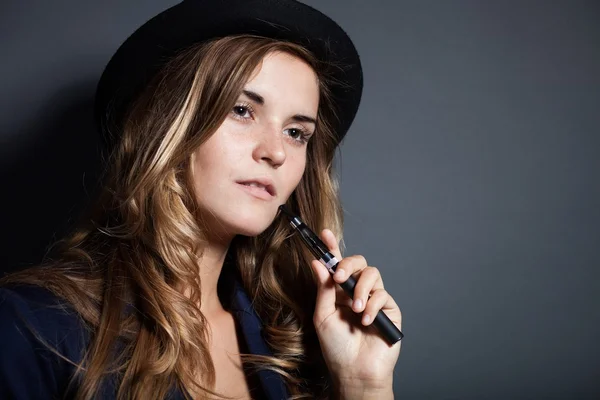 Elegante mujer fumando cigarrillo electrónico con traje y sombrero —  Fotos de Stock