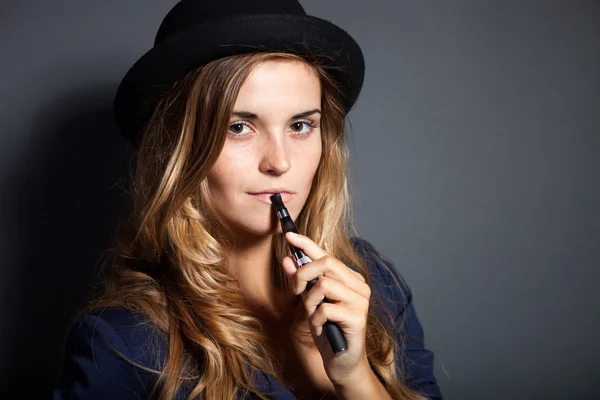 Элегантная женщина, курящая электронную сигарету в костюме и шляпе — стоковое фото