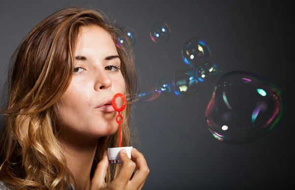 Beautiful young girl blowing soap bubbles, dark background — Stock Photo, Image