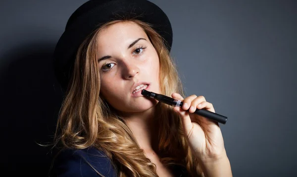 Elegante donna che fuma e-sigaretta indossando abito e cappello — Foto Stock