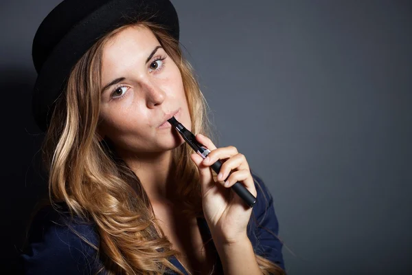 Elegant woman smoking e-cigarette wearing suit and hat — Stock Photo, Image