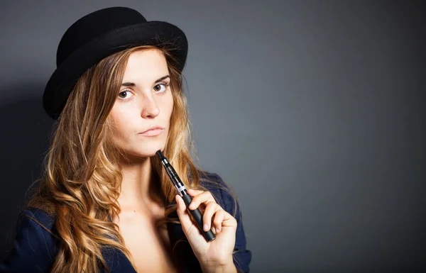 Elegante mujer fumando cigarrillo electrónico con traje y sombrero —  Fotos de Stock