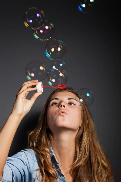 Mooi meisje blazen van zeepbellen, donkere achtergrond — Stockfoto