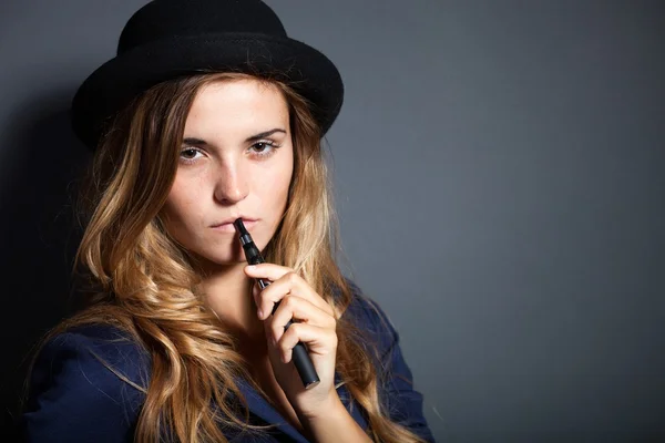 Elegante donna che fuma e-sigaretta indossando abito e cappello — Foto Stock