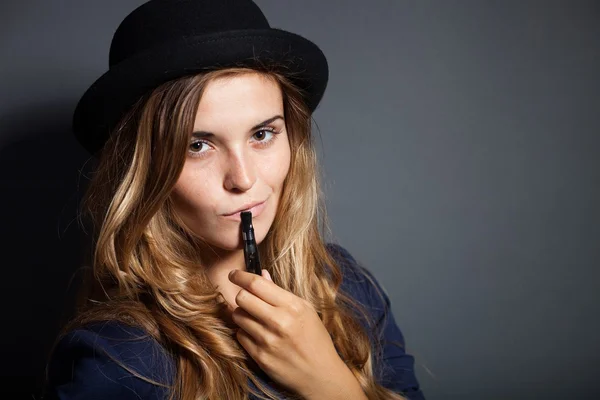 Elegante mujer fumando cigarrillo electrónico con traje y sombrero —  Fotos de Stock