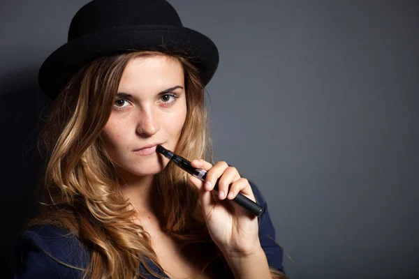 Elegante mujer fumando cigarrillo electrónico con traje y sombrero —  Fotos de Stock