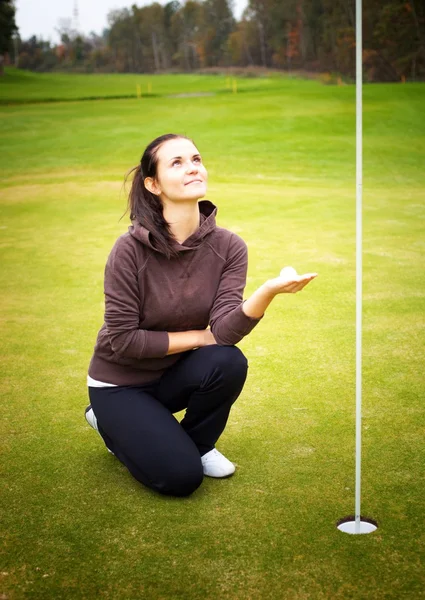 Ung kvinna golf spelare hålla bollen tittar på cup flaggan — Stockfoto
