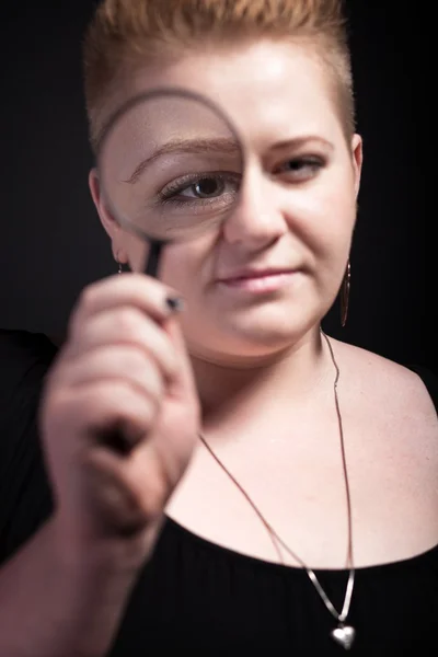 Mollige vrouw met kort haar kijken door een vergrootglas — Stockfoto