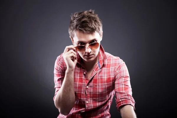 Beau jeune homme avec des lunettes de soleil sur fond sombre — Photo