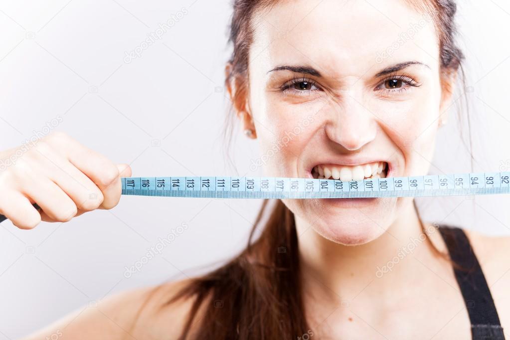 Angry young woman biting measuring tape