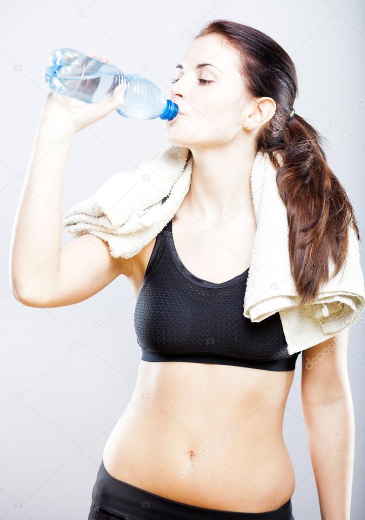 Young natural woman drinking water after fitness training