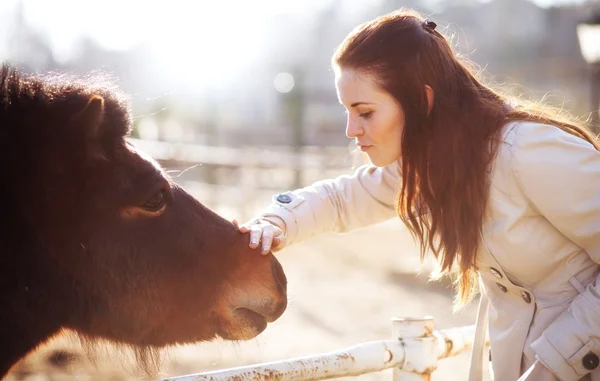 Wanita muda membelai kuda poni di kebun binatang mini — Stok Foto