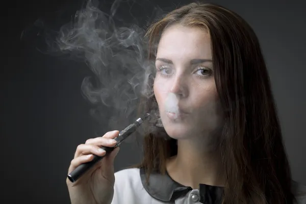 Elegante mujer fumando cigarrillo electrónico con humo — Foto de Stock