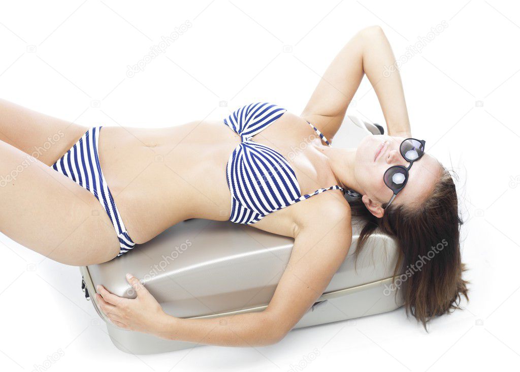 Tourist woman in bikini laying on suitcase