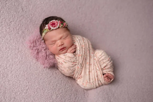 Little newborn Ukrainian girl sleeps peacefully on a pink background. On his head a bandage of flowers. Royaltyfria Stockfoton