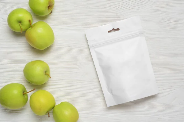 White plastic pouch bag with apples on wood table. Mock-up template for design. 3d rendering illustration.