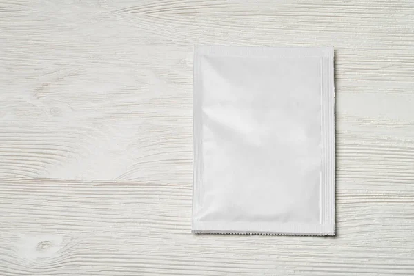 White blank paper sachet packet on wood table. Mock-up template for design.