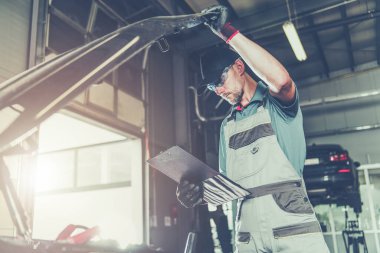 Caucasian Car Mechanic Electronic Elements Technician Checking on an Issue with a Vehicle Looking Under Its Hood. Automotive Service Industry.