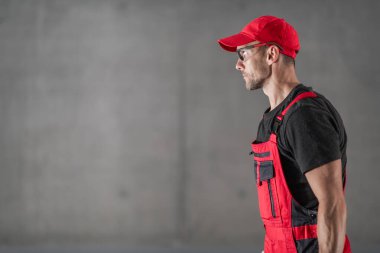 Industrial Caucasian Worker in His 40s Wearing Safety Glasses and Hat. Raw Concrete Wall in a Background. Industrial Theme.