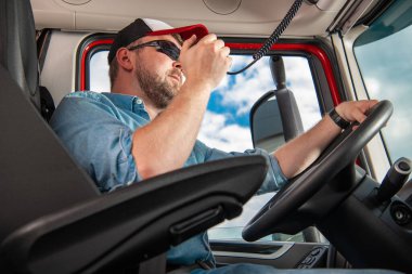 Semi Truck Lorry Driver Talking on CB Radio While Driving in Modern Semi Trailer Truck. Transportation Industry Theme.