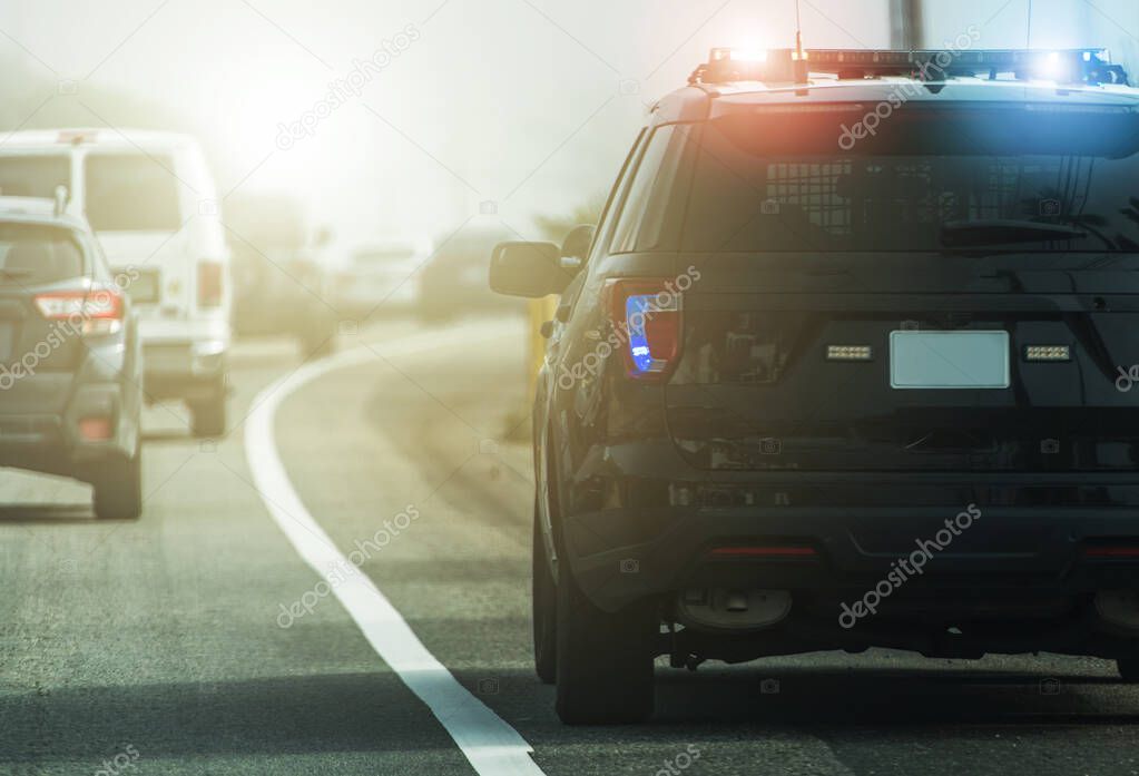 Flashing Lights of American Modern Highway Police Patrol Cruiser on Side of a Road. Rear View. Transportation and Police Enforcement Theme.