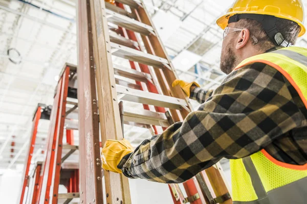 ハイテーマで働くためにはしごを取る黄色のハードハットを身に着けている白人労働者 建設業 — ストック写真