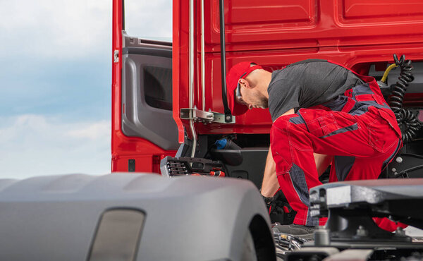 Professional Caucasian Truck Mechanic in His 40s Wearing Red Uniform Performing Modern Semi Truck Repair. Transportation Industry.