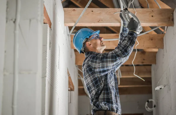 40代の白人プロ電気技師木製梁屋根構造を持つ新しく開発されたコンクリートレンガ造りの家の中に天井照明ポイントを設置 — ストック写真