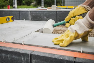 Patio Concrete Tiles Floor Paving. Landscaping Worker with Soft Hammer Adjusting Concrete Tile. 